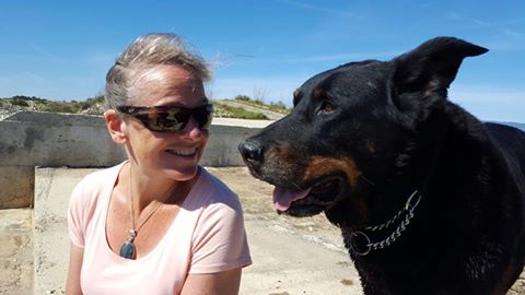 Vrouw met grijs haar in roze tshirt kijkt naar een grote zwarte hond