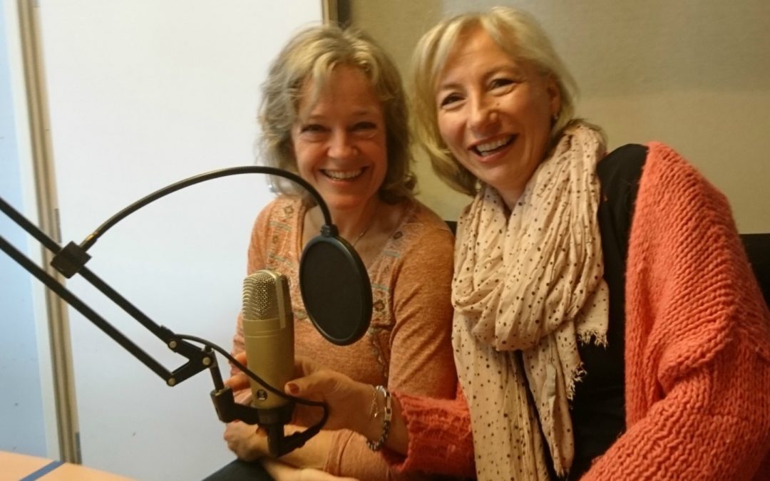 Linda Spaanbroek Angela Mastwijk twee lachende vrouwen met grijs haar die achter een podcastmicrofoon zitten