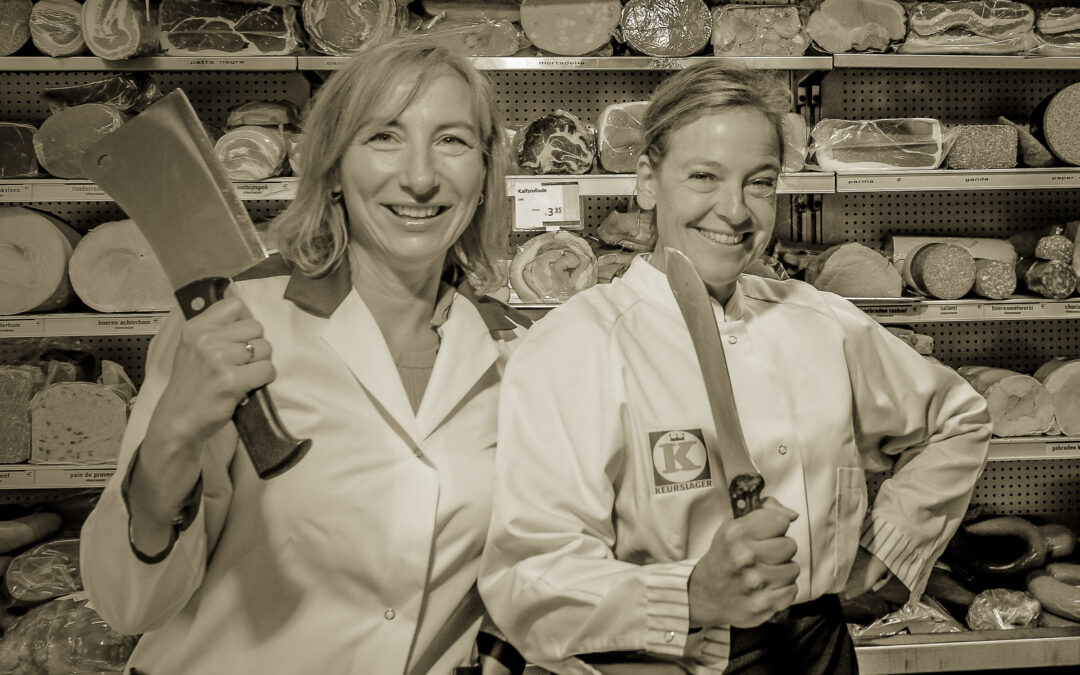 Slagersdochters Linda Spaanbroek en Angela Mastwijk poseren in een slagerij met messen in hun handen