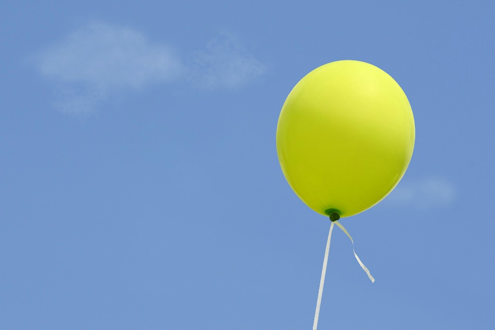 Gele ballon aan wit lintje voor blauwe lucht