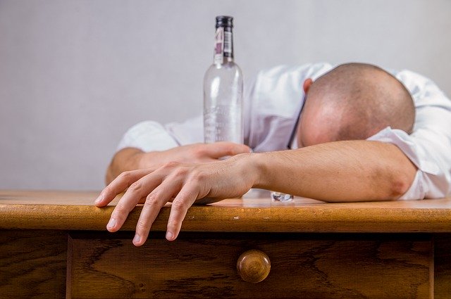 man ligt dronken over tafel met een fles in zijn handen ongemakkelijke gevoelens wegdrinken