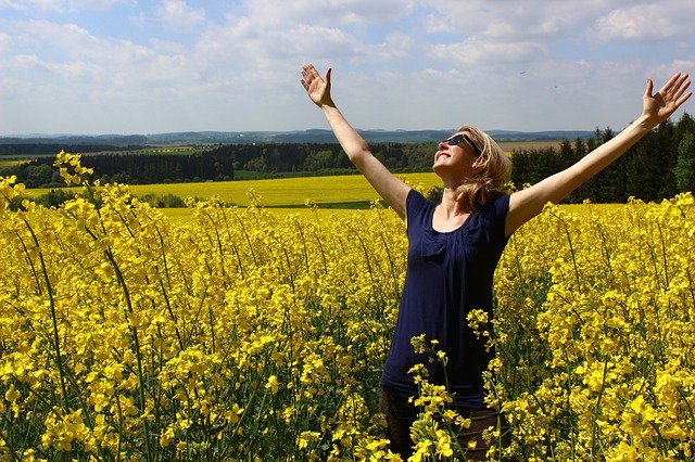 Vrouw in veld met gele bloemen aanbid de zon dankbaar voor de 3 Principes van creatie