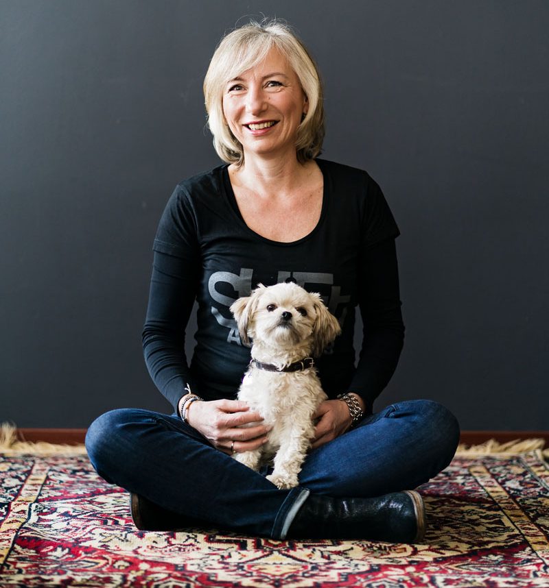 Linda Spaanbroek vrouw met grijs haar in een zwarte jurk met een witte streep om de hals met mobiel in haar handen