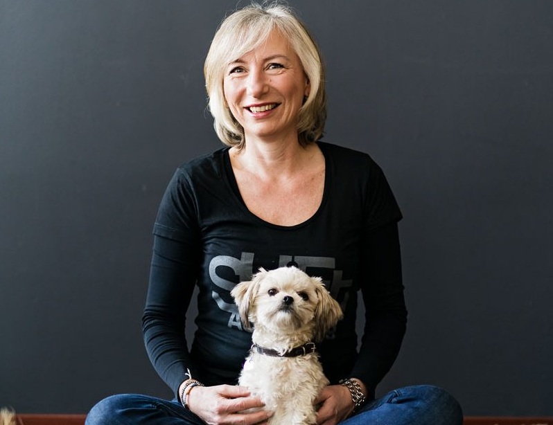 Linda Spaanbroek vrouw met grijs haar in een zwarte jurk met een witte streep om de hals met mobiel in haar handen